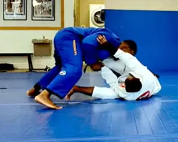 Two grapplers training at an academy, one in a blue gi passing the guard of one in a white gi